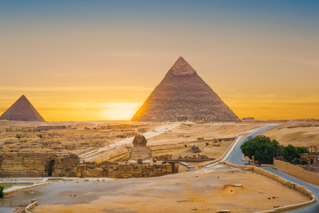 Voyage organisé en Égypte – Pyramides de Gizeh au coucher du soleil Pyramides de Gizeh en Égypte au coucher du soleil, vues lors d’un voyage organisé en Égypte depuis le Maroc, avec désert doré et ciel lumineux.