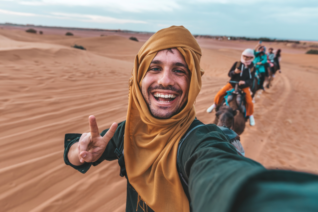 Dubaï – Aventure dans le désert, voyage organisé depuis le Maroc Voyageur prenant un selfie dans le désert de Dubaï avec une caravane de chameaux, une des destinations plus demandées au Maroc, populaire pour le voyage et le voyage organisé depuis le Maroc.