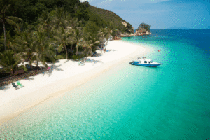 Plage tropicale de Malaisie avec sable blanc, eau turquoise et bateau proche du rivage — destination idéale d’un voyage organisé en Malaisie avec Colibri Voyage.