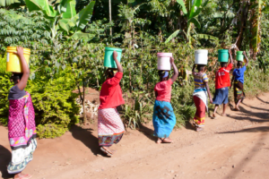 Femmes marchant sur un chemin rural avec des seaux, scène authentique d’Afrique de l’Est lors d’un voyage ou d’un voyage organisé.