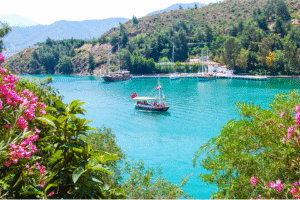 Baie turquoise en Turquie avec voiliers et yacht entourée de collines et fleurs roses, idéale pour un voyage organisé.