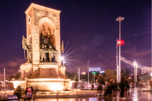 Monument de la République à Istanbul illuminé la nuit avec drapeau turc, idéal pour un voyage organisé ou un voyage en Turquie.