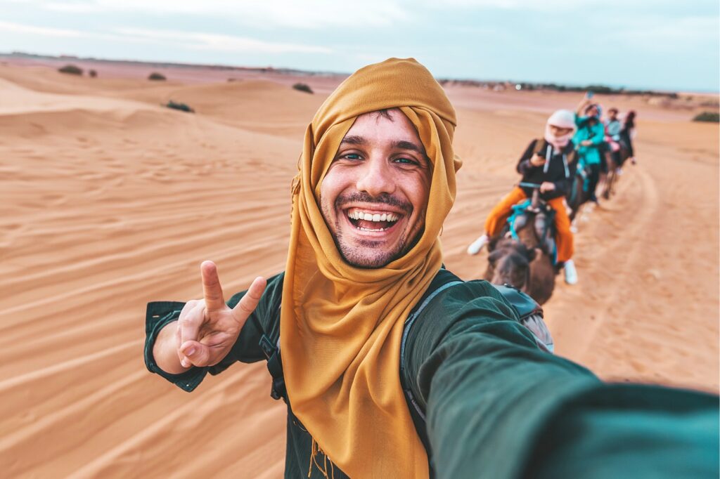 Voyageur prenant un selfie dans le désert de Dubaï avec une caravane de chameaux, une des destinations plus demandées au Maroc, populaire pour le voyage et le voyage organisé depuis le Maroc.