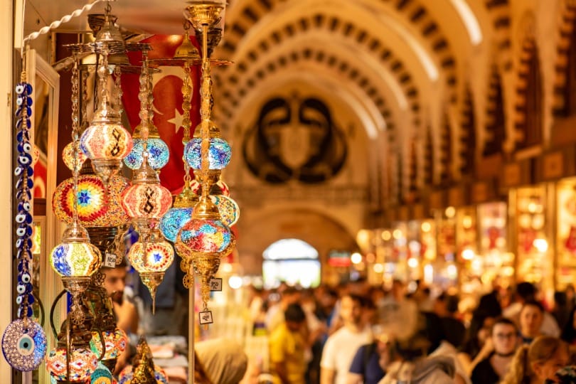 Lampes turques colorées en mosaïque suspendues dans un bazar animé avec drapeau turc, symbole d'un voyage organisé en Turquie ou d'un voyage individuel.